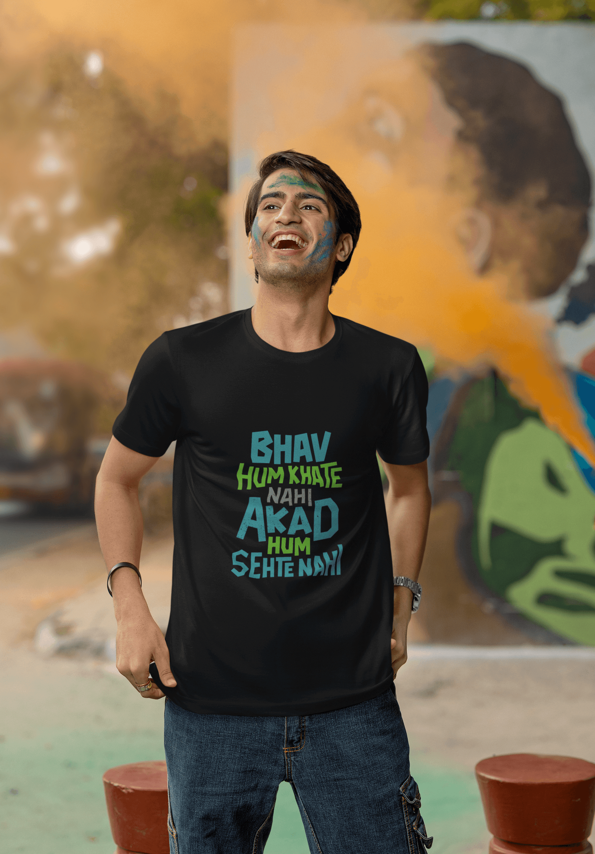 Man wearing BHAV HUM KHAATE NAHI unisex t-shirt outdoors, vibrant colors in background.