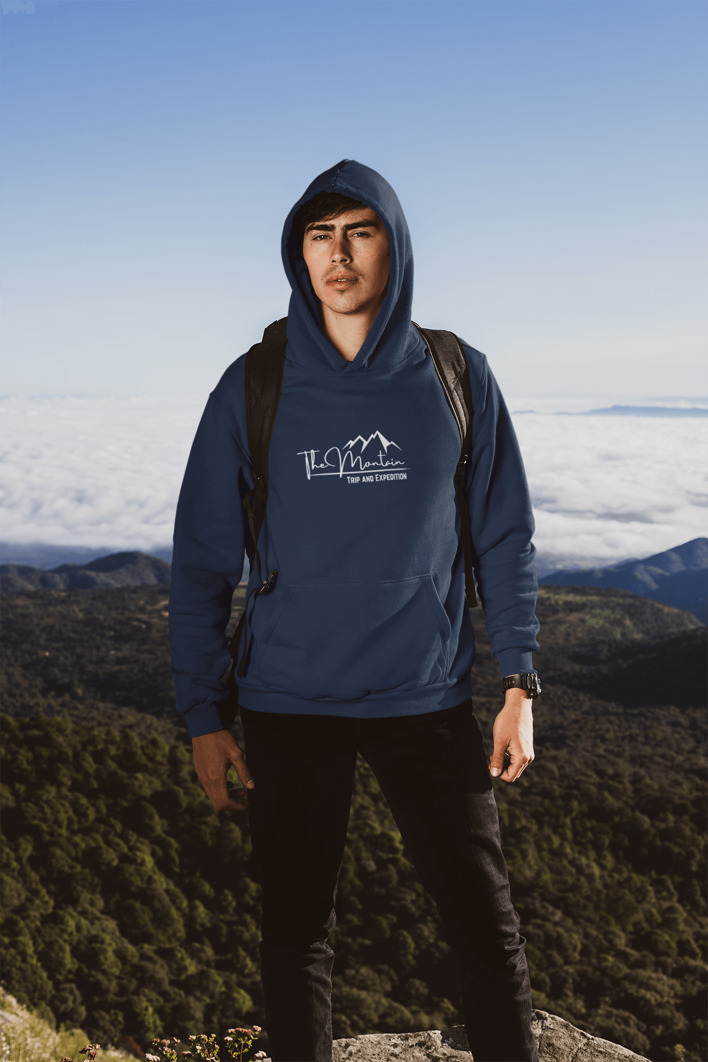 Man wearing a navy hooded sweatshirt stands outdoors against a stunning mountain backdrop, showcasing adventure and style.