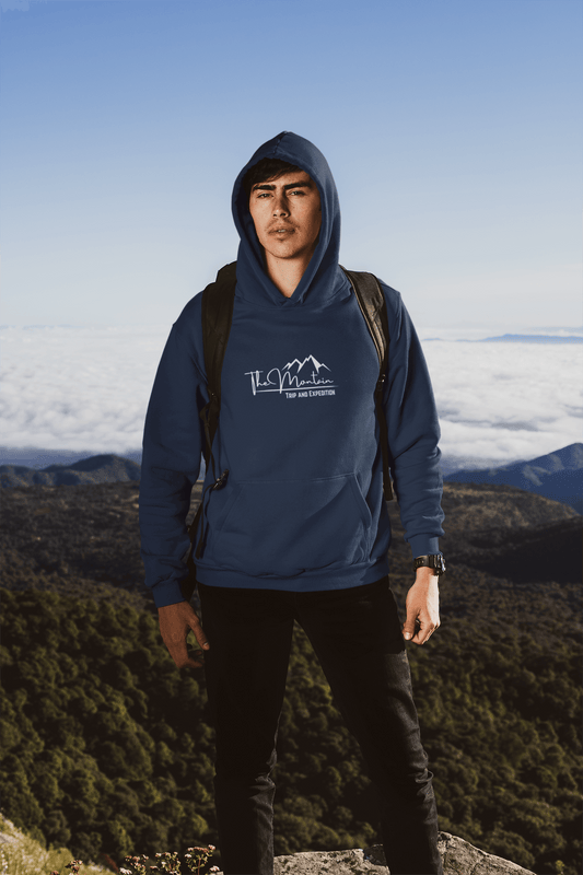 Man wearing a navy hooded sweatshirt stands outdoors against a stunning mountain backdrop, showcasing adventure and style.