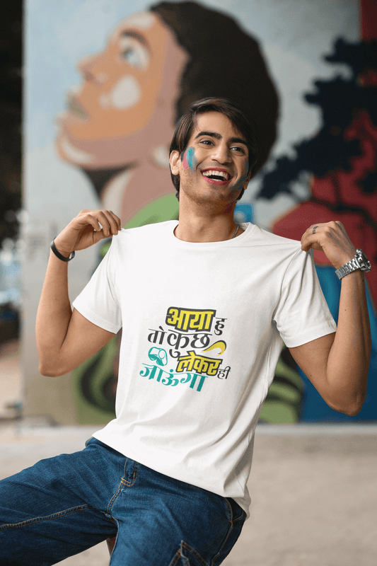 Man wearing AYA HU KUCH TOH LEKE JAUNGA unisex t-shirt with colorful design, sitting and smiling in front of a mural.